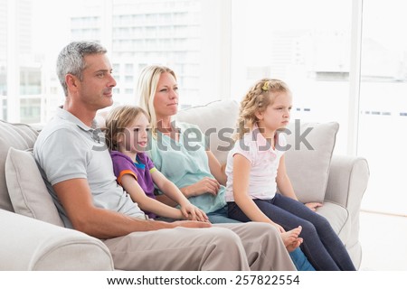 Family of four watching TV while sitting on sofa at home