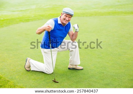 Smiling golfer kneeling on the putting green on a sunny day at the golf course