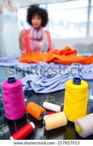 Close up of threads on table with female fashion designer in background