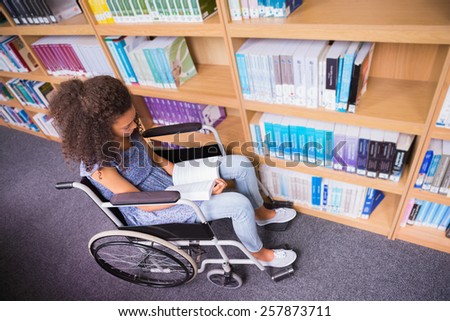 Smiling disabled student in library reading book at the university