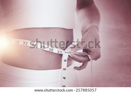 Closeup midsection of woman measuring waist against black wall