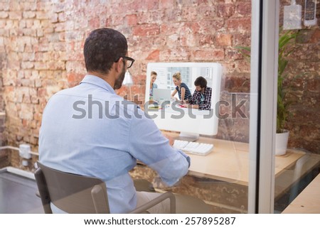 Casual business people around conference table in office against businessman using computer at desk