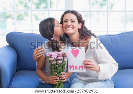 Cute girl offering flowers and card to her mother in the living room