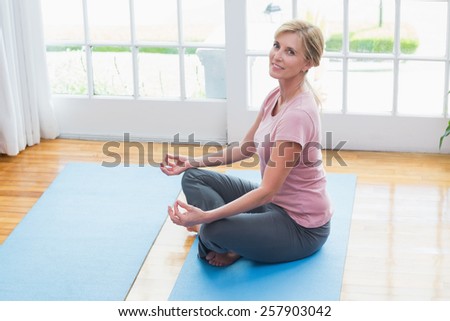 Mature woman doing yoga on fitness mat at home in the living room