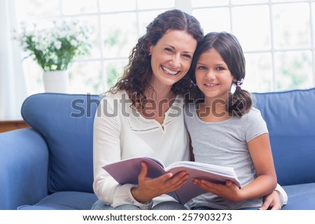 Happy mother and daughter sitting on the couch and reading book in the living room