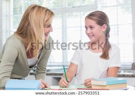 Happy mother helping daughter doing homework at home in the kitchen