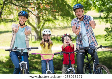 Happy family on their bike with thumbs up at the park on a sunny day