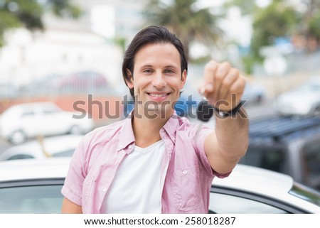 Young man smiling and holding key in front of his car