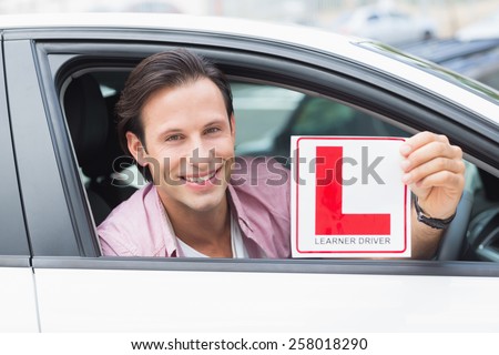 Learner driver smiling and holding l plate in his car
