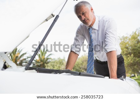 Upset man checking his car engine after breaking down on the road