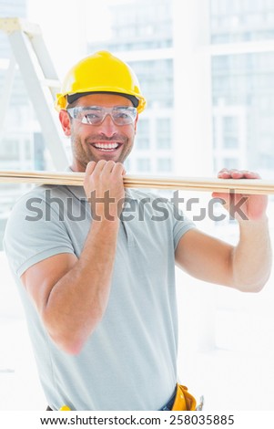 Portrait of happy carpenter carrying wood in building