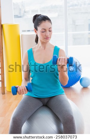 Young woman exercising with dumbbells on fitness ball in fitness studio