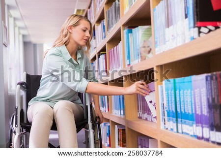 Smiling disabled student in library picking book at the university