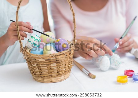 Happy mother and daughter painting easter eggs in the living room