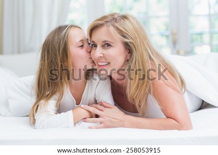 Daughter kissing her mother on the cheek in the bed at home in the bedroom