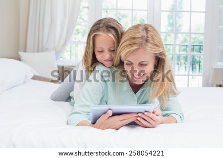 Happy mother and daughter using tablet in bed