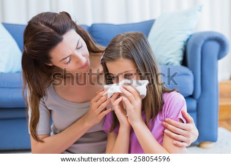 Mother helping daughter blow her nose at home in the living room