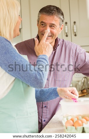 Happy woman putting flour on husbands nose at home in the kitchen