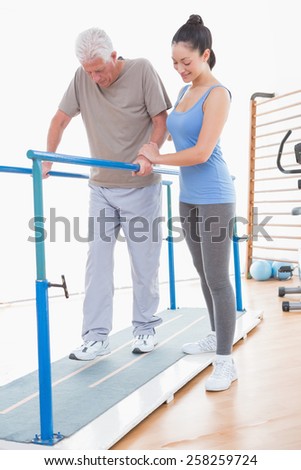 Senior man walking with parallel bars and coach help in fitness studio