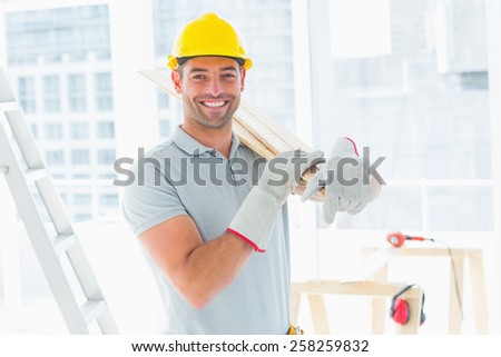 Portrait of smiling manual worker carrying planks in building