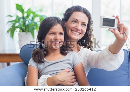 Happy mother and daughter sitting on the couch and taking selfie in the living room