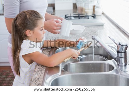 Mother and daughter washing up at home in kitchen