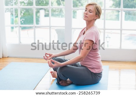 Mature woman doing yoga on fitness mat at home in the living room
