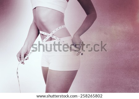 Midsection of woman measuring waist against black wall