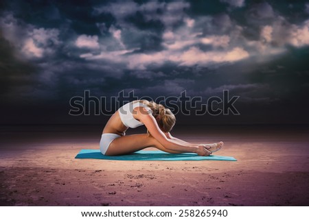 Gorgeous fit blonde in seated forward bend pose against dark cloudy sky
