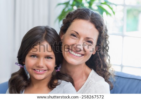 Happy mother and daughter sitting on the couch and smiling at camera in the living room