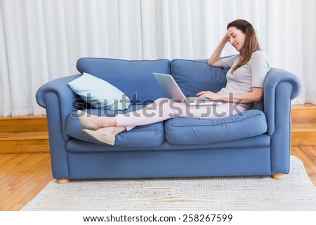Casual woman using laptop on couch at home in the living room