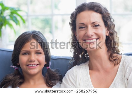 Happy mother and daughter sitting on the couch and smiling at camera in the living room