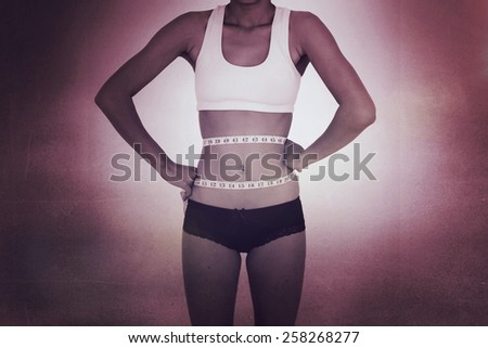 Surprised slim woman measuring her waist against black wall