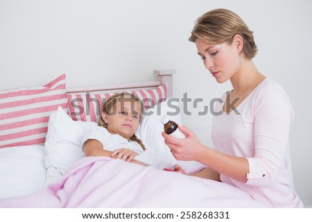 Mother about to give medicine to sick daughter at home in the bedroom