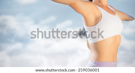 Sporty blonde standing on the beach with arms out against mountain peak through the clouds