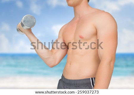 Strong man lifting dumbbell with no shirt on against beach scene