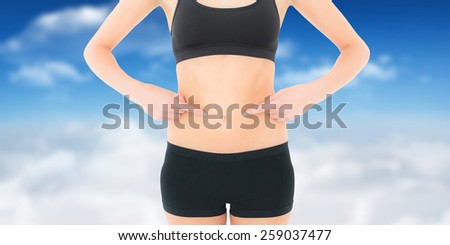 Closeup mid section of a fit woman with hands on stomach against bright blue sky with clouds