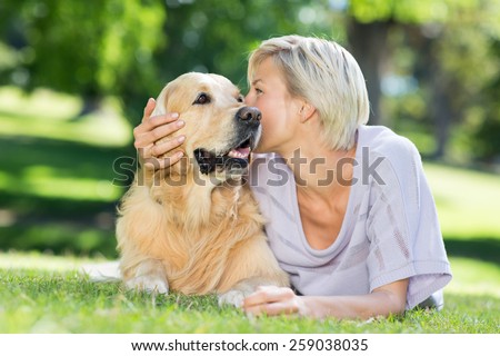 Pretty blonde kissing her dog in the park on a sunny day
