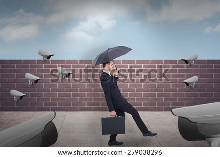 Businessman holding briefcase under umbrella against blue sky over a brick wall