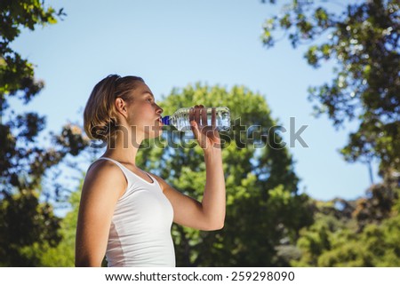 Fit woman drinking water in park on a sunny day