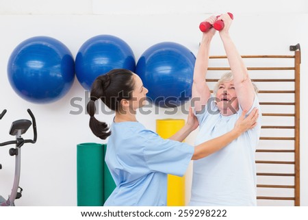 Therapist helping senior woman fit dumbbells in fitness studio