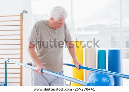 Senior man walking with parallel bars in fitness studio