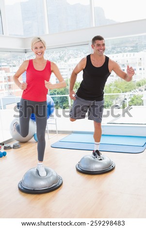 Fit couple working on bosu ball in fitness studio