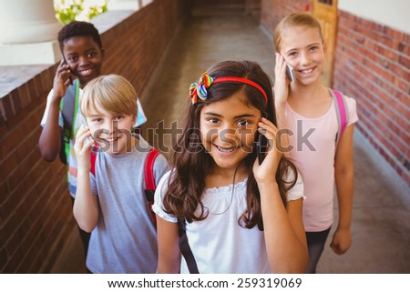 Portrait of smiling little school kids using cellphones in school corridor
