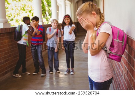 Side view of sad schoolgirl with friends in background at school corridor