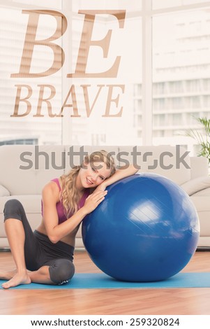Fit blonde sitting beside exercise ball smiling at camera against be brave