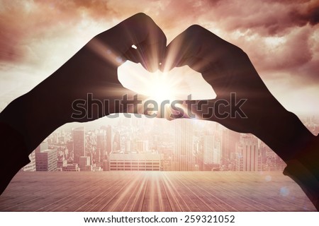 Woman making heart shape with hands against balcony overlooking city