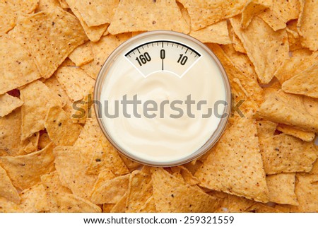weighing scales against bowl of dip placed among nachos