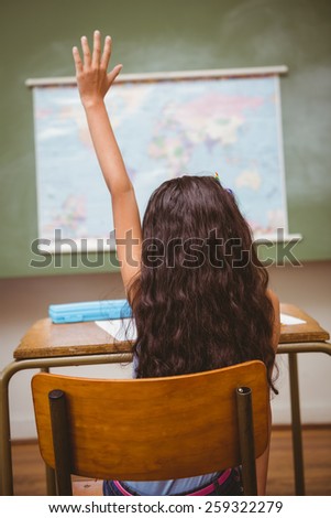Rear view of little girl raising hand in the classroom