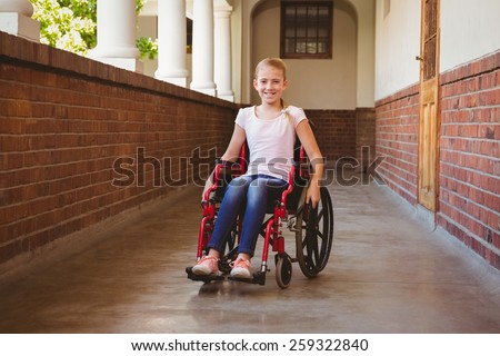 Portrait of cute little girl sitting in wheelchair in school corridor